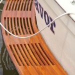 Curved wooden bench with slats next to a boat.